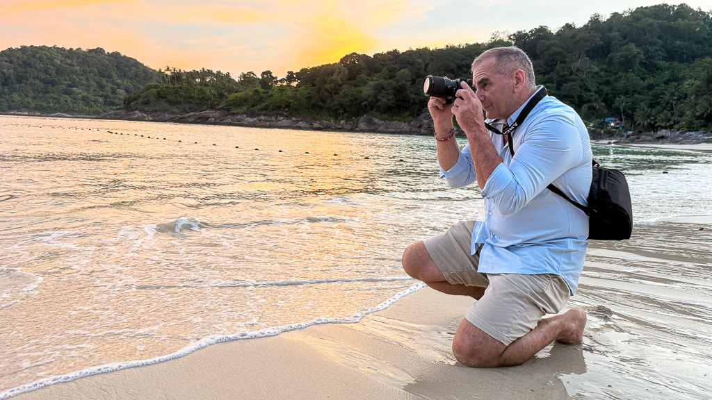 Reflections Photography – Sunrise Beach Shoot in Phuket, Thailand Man sitting on a beach at sunrise in Phuket, Thailand, capturing a tranquil moment with soft golden light — hero image for Reflections Photography.