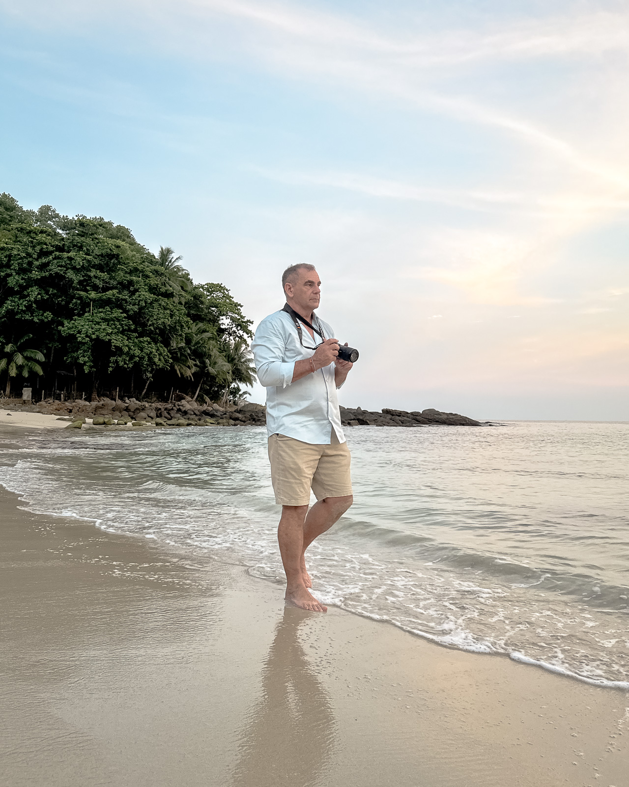 Dave Hibbins at Freedom Beach – Phuket Author Portrait Dave Hibbins walks barefoot along Freedom Beach in Phuket, holding a camera and reflecting during golden hour.