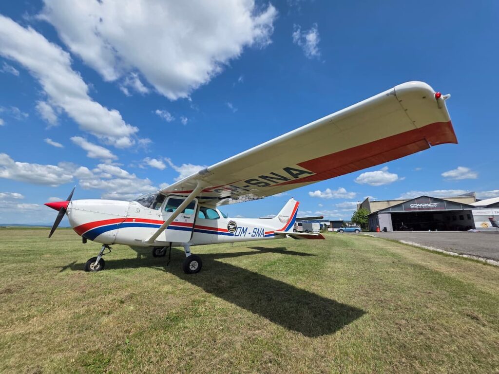 Small Cessna aircraft parked on grass beside an airfield under a bright blue sky.
